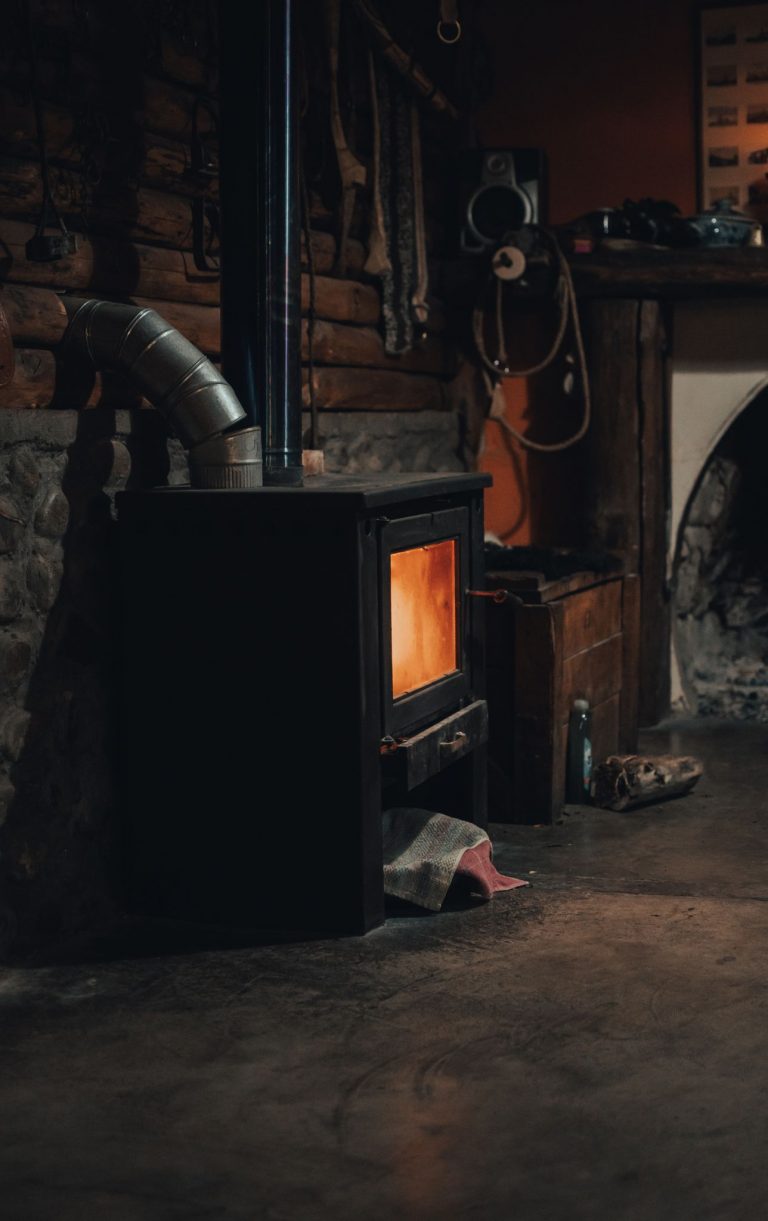 Warm and inviting indoor scene featuring a rustic wood-burning stove against a brick wall.